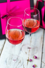 Two glasses of rose wine on white wooden table with pink gift boxes on background
