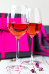 Two glasses of rose wine on white wooden table with pink gift boxes on background