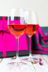 Two glasses of rose wine on white wooden table with pink gift boxes on background