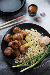 Black plate with rice and meatballs cooked in chinese style, studio shot on a light-grey stone background