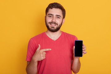 Close up portrait of young happy man in red shirt showing black blank smart phone screen, looking...