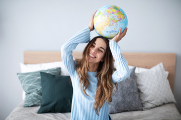 Young joyful woman dreaming of a travel holding a model globe above her head.