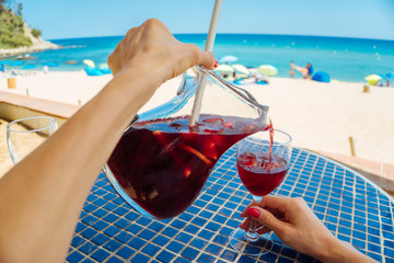 POV image of female hands pouring fresh red wine sangria into a glass - relax, vacation, leisure,...