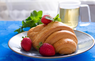 Tasty croissant with  fresh strawberries and green tea on blue cement background.Side view.