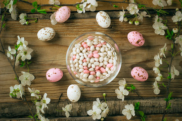 branch of spring flowers and colorful pink candy eggs for easter on rustic background
