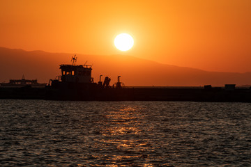 Amazing sunset in the mountains around Izmir. Taken at the waterfront in Konak district with the silhouette of a boat and the ocean.