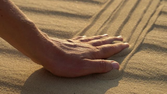Woman hand tuoching sand on the beach or desert in sunset lights. UHD, 4K