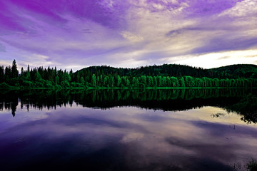 Wooded river shore and purple sky that are reflected in the water