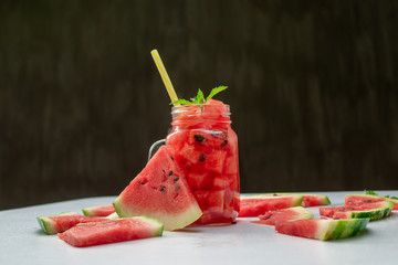 Summer watermelon drink in glass and slices of watermelon on dark background