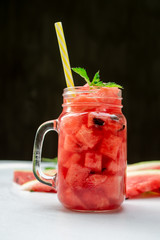 Summer watermelon drink in glass and slices of watermelon on dark background