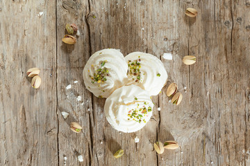 White marshmallows on old wooden background decorated with pistachios. Top view