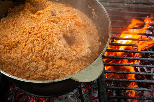 Pilaf cooking on fire outdoor. Open air kitchen at party picnic. Big pot with dish of rice and meat stays on wire rack and steams. Close up image of meal dish preparation
