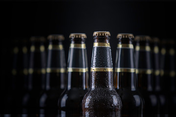 Beer bottles with blank labels lined up in selective focus on black background, one with frost...