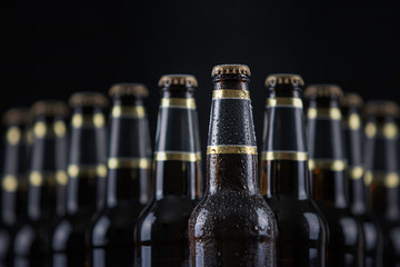 Beer bottles with blank labels lined up in selective focus on black background, one with frost...