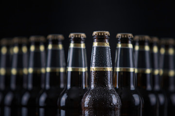 Beer bottles with blank labels lined up in selective focus on black background, one with frost...