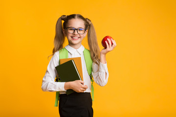 Little School Girl Holding Apple And Books On Yellow Background
