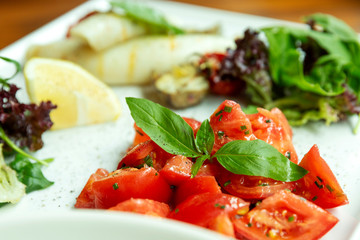 Sliced tomatoes with basil and lettuce in a plate. Beautiful food design. Close-up.