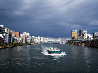 Fototapeta na wymiar 夏の曇り空の東京隅田川を行く船と川沿いの町の風景　8月