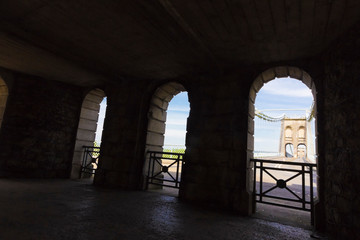 Creative view from an open-air stone covered undercover walkway looking out onto the Menai Suspension Bridge & A5 traffic route, North Wales