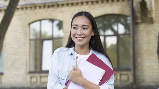 Portrait of happy, smiling student girl sitting on the beanch. Looking aside, and then looking at the camera. Handheld shot.