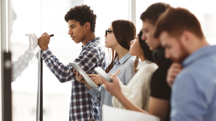 Student boy writing answers to tasks on whiteboard in class