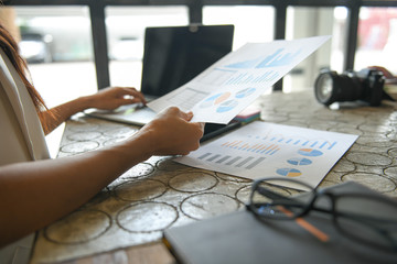 Hand of a business woman is using a laptop to find information.She hold the graph and put her hand on laptop keyboard.