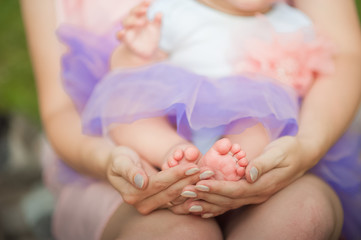 Female hands hold the legs of a child close-up. Beautiful conceptual image of Maternity. Mom and baby, happy Family concept. Baby feet in her mother hand.