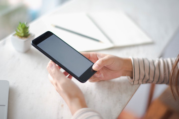 Closed up and focus on hand of young woman using a smartphone which show white display and have note book put on table in near. co working space concept.
