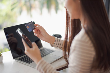 Closed up and focus on hand of young woman hold a credit card and other hand using a smart phone which is shopping online and sitting on table near big mirror at cafe. online payment concept.