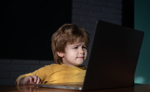 Child is bored at the computer at night in the dark. Seated child using a laptop. A young boy child is looking at a laptop with math, science and animals information. School, study, learning concept.