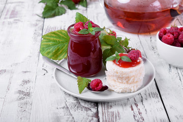 Raspberry jam on pieces of white wheat bread and freshly brewed tea on white wooden table