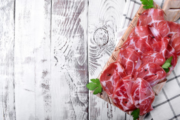 Thin slices of Italian cold cut pork Coppa on white wooden table