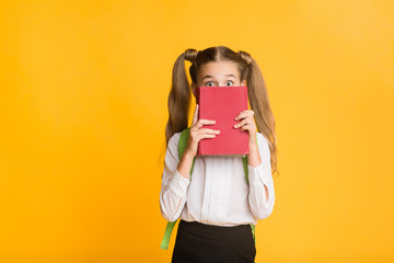 Scared Schoolgirl Hiding Behind Book On Yellow Studio Background