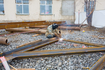 Welder in mask welding metal construction on open air.