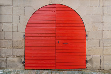 Rotes, frisch gestrichenes rundes Holztor in einer alten Fassade aus Stein