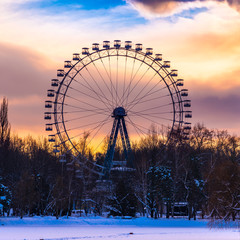 Beautiful winter park landscape - Ferris wheel in a park on the shore of a frozen pond at sunset