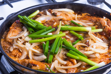 Pieces of pork fried in a pan with hot sauce and onions, close-up