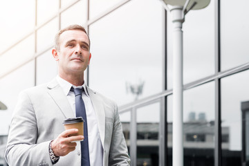 Be ambitious. Businessman in suit is walking along the building with take-out coffee. Copy space on the right side