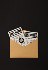 Envelope with FAKE NEWS newspapers over black