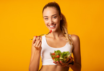 Slim Young Woman Eating Salad From Bowl On Yellow Background