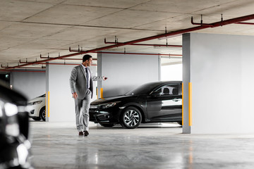 Quick and comfortable. Businessman in grey suit parks his car at parking lot. Copy space on the right side - obrazy, fototapety, plakaty