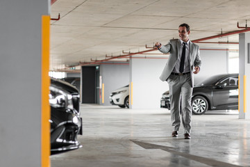 Spacious area. Businessman in grey suit parks his car at parking lot. Copy space on the left side