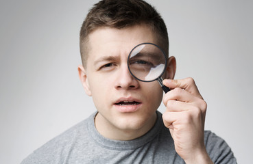 Fototapeta na wymiar Curious young man looking through magnifying glass