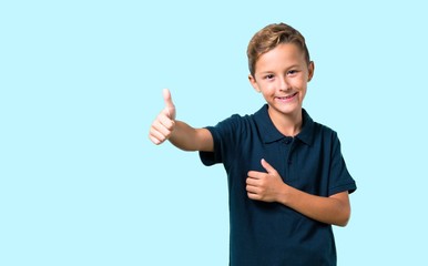 Little boy giving a thumbs up gesture and smiling on blue background