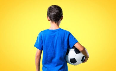 Boy playing soccer in back position on yellow background © luismolinero