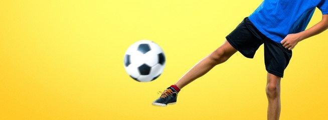 Boy playing soccer kicking the ball on yellow background