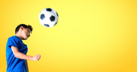 Boy playing soccer hitting the ball with the head on yellow background