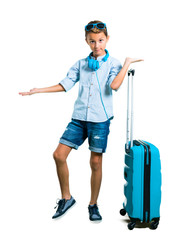 Full body of Kid with sunglasses and headphones traveling with his suitcase holding copyspace imaginary on the palm on isolated white background