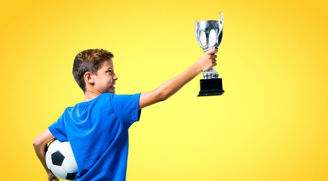 Boy Playing Soccer And Holding A Trophy On Yellow Background