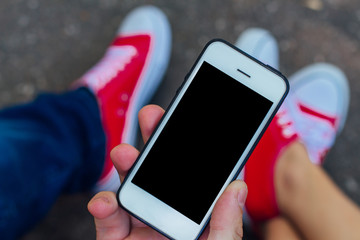 Hand holding mobile phone with blacj screen on background of red sneakers shoes on woman's and man's feet.